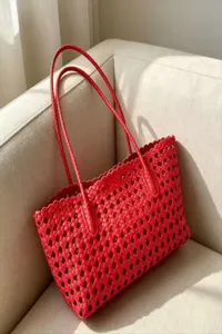 Close-up detail of the red woven cutout tote bag showing premium texture and double straps.