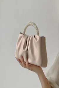 Close-up detail of stylish pleated beige handbag with elegant faux pearl handle design.
