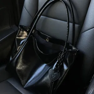 Black glossy leather tote bag detail showing heart-shaped charm and double straps.