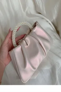 Close-up detail of a glamorous pleated cloud handbag with elegant faux pearl beaded handle.