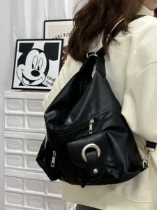 Detail shot of a black PU leather multiway backpack with zipper pockets and metal ring.