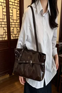 Women brown patent leather shoulder bag, stylish motorcycle style tote with buckle details.
