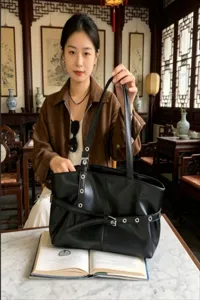 Detailed view of the black leather shoulder bag with metal eyelets and belt detail.