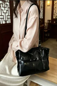 Black leather motorcycle style shoulder bag underarm tote with metal buckle and grommets.