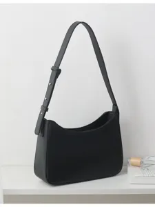 Detailed view of black minimalist shoulder bag with adjustable strap on clean white surface.