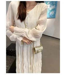 Detail view of a luxury gold quilted mini chain crossbody bag paired with white dress.