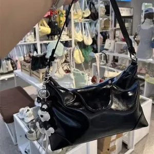 Black patent leather shoulder dumpling bag detail view, chic minimalist hobo design.