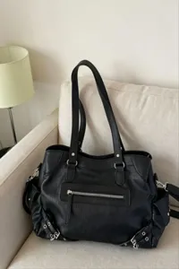 Detail shot of black leather shoulder bag with zipper pocket and metal buckle accents.