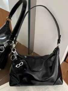Black patent leather shoulder bag for women featuring trendy glasses pendant and strap.