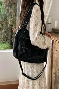 Detailed shot of a large black leather motorcycle shoulder bag with multiple metal zippers.