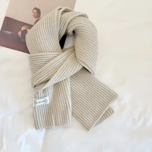Beige knitted scarf detail shot showing soft ribbed texture and neat brand label design.