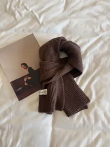 Detailed close-up of a dark brown knitted winter scarf with ribbed texture and tag.