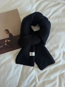 Close up of black knitted winter scarf with brand tag laid neatly on soft white fabric.