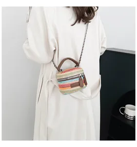 Detailansicht der bunten gestreiften Stroh-Eimer-Tasche mit braunem Griff und Kette.