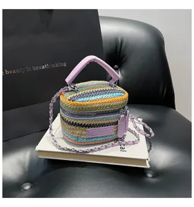 Bunte Stroh-Umhängetasche mit Kontraststreifen, violettem Griff und Kettengurt.