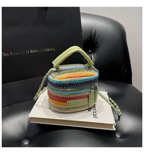 Detailansicht der bunten gestreiften Stroh Eimer Tasche mit grünem Ledergriff und Kette.