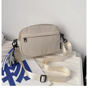 Vue détaillée du sac bandoulière beige décontracté avec poche zippée et breloque élégante.