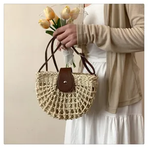Handheld woven straw bag detail showing the hollow-out pattern and leather flap closure.
