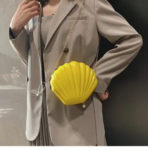 Dettaglio di una borsa a tracolla a forma di conchiglia in vernice gialla con catena.