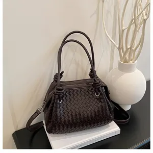 Close-up detail of a dark brown woven leather handbag on a white book with elegant decor.