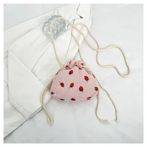 Close-up of pink corduroy strawberry print mini bucket bag with white drawstring straps.
