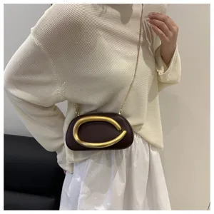 Mini sac bandoulière marron de soirée avec détail de boucle dorée porté par le mannequin.