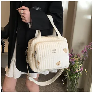 Primer plano del bolso de hombro acolchado blanco con bordado de osito y correas dobles.