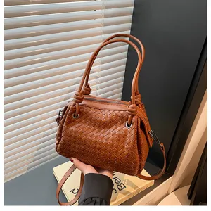 Close-up detail view of stylish brown woven leather shoulder handbag with metal rings and knots.