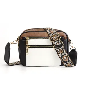 Detail view of stylish colorblock crossbody bag with ethnic guitar strap and gold zippers.