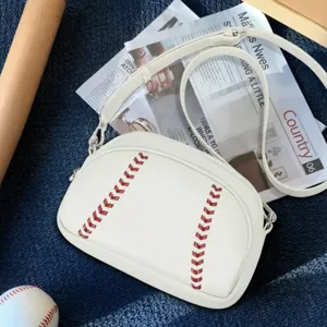 White leather baseball crossbody bag with red stitching and zipper shoulder strap detail.