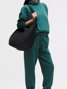 Detail view of a large black nylon crescent crossbody bag worn by a model in green.