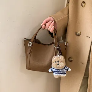 Detail shot of retro litchi pattern PU bucket bag with cute bear pendant and metal hardware.