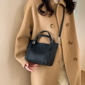 Detail shot of black pebbled PU bucket bag with top handles, silver hardware and strap.