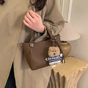 Close-up of brown PU bucket bag with cute plush bear charm, showcasing detailed leather texture.