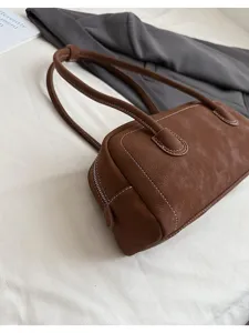 Detailed view of the brown leather baguette shoulder bag featuring white contrast stitching texture.