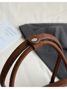 Brown leather handbag handle detail shot with white stitching and snap button closure.
