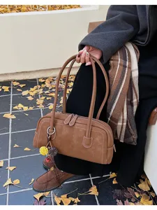 Detailed view of brown retro baguette shoulder bag with contrast stitching and charming pendant.