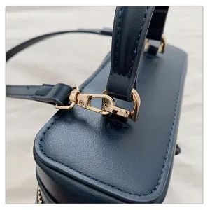 Close-up detail shot of dark blue leather box bag featuring polished gold hardware and stitching.