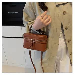 Close-up view of a brown vintage vanity box handbag featuring dual zippers and tassel accents.