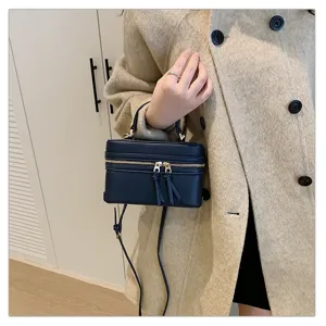 Close-up of a stylish dark blue vanity box bag with zipper and tassels held by hand.