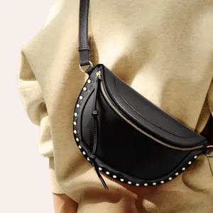Detailed view of a stylish black crescent crossbody bag with metallic studs worn across the body.