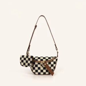 Detailed view of black and white checkered canvas crossbody bag with brown leather strap.