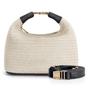Woven straw handbag detail showing premium texture, black leather handles and gold metal hardware.