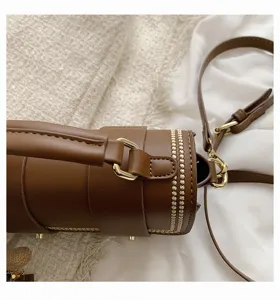 Detailopname van een retro bruine cilindrische handtas met gouden hardware en stiksels.