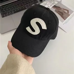 Black cotton baseball cap detail showing white letter S embroidery and brim stitching.