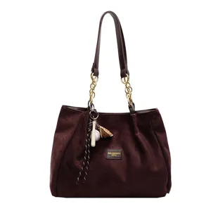 Brown suede tote bag close-up showing soft texture, chain strap and baseball pendant.