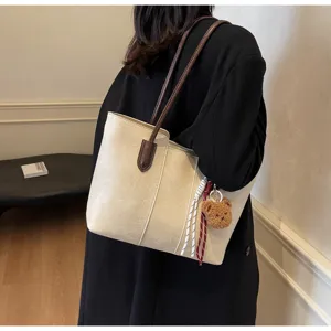 Beige leather tote shoulder bag detail view with brown straps and cute bear charm.