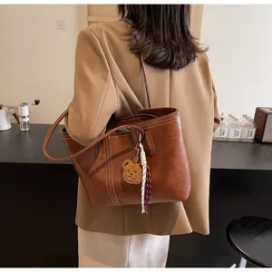 Detailed view of brown vintage leather tote bag with contrast stitching and cute bear pendant.