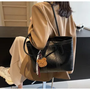 Detailed view of black large capacity shoulder tote bag with white stitching and cute bear charm.
