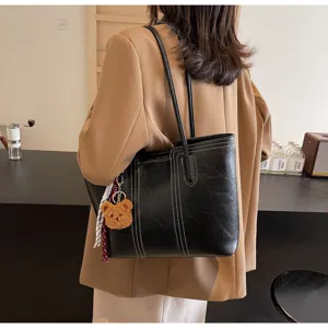 Detailed view of black PU leather tote bag with white stitching and cute bear charm pendant.